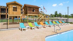 A poolside area with lounge chairs, a wooden building, and American flags.