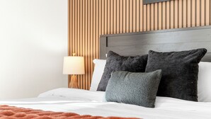 A neatly made bed with a brown blanket, a wooden headboard, and a wall-mounted TV.