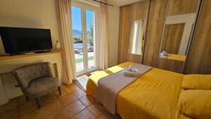 Habitació d'hotel amb un llit, una cadira, un televisor i una porta corredissa de vidre que dona a una zona exterior.