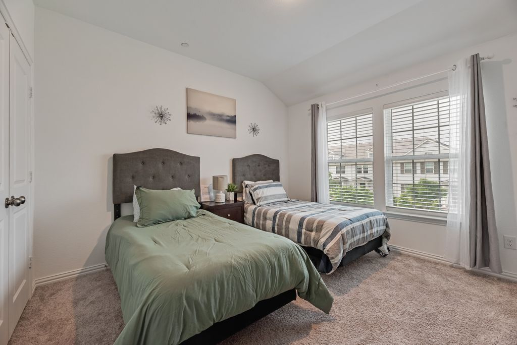 A bedroom with two beds, a window with blinds, a door, and a wall-mounted artwork.