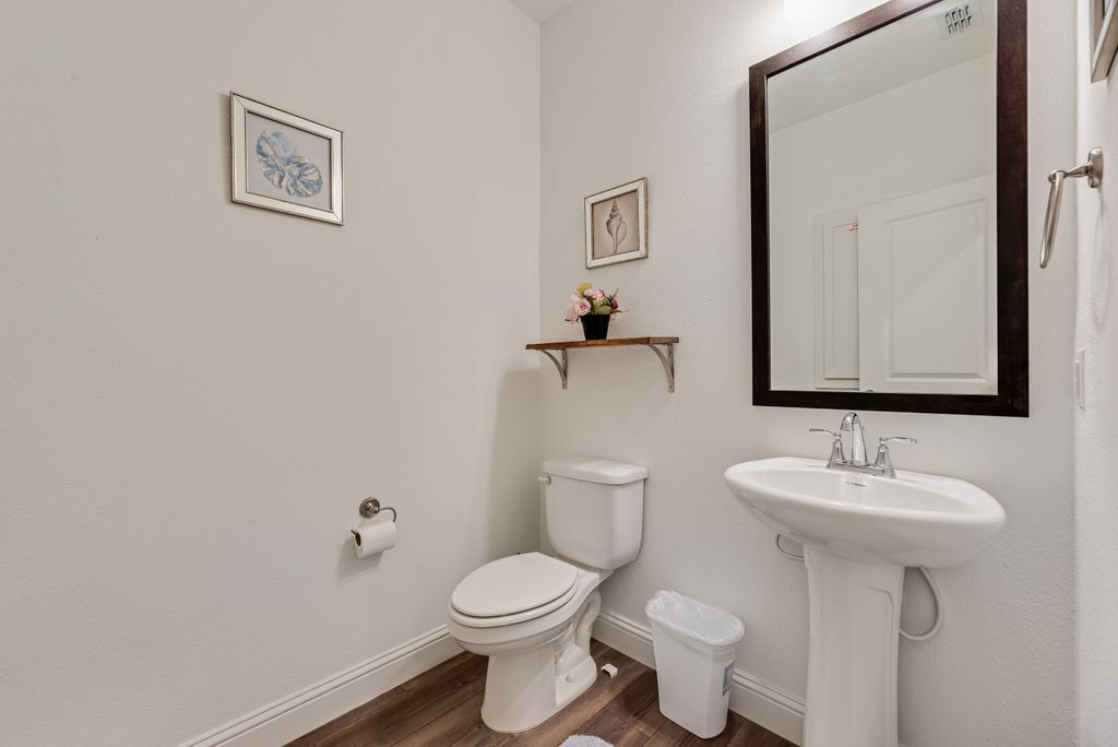 A bathroom with a toilet, sink, and mirror. There are two framed pictures on the wall.