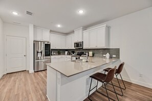 Una cocina moderna con armarios blancos, electrodomésticos de acero inoxidable y una isla grande con taburetes de bar.