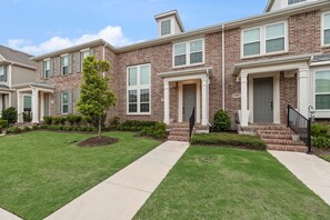 A row of two-story brick townhouses with front porches, a central tree, and a sidewalk. - FS832 | Frisco Retreat | 2BD | Universal Kids Resort (Frisco)
