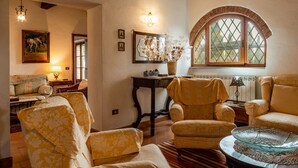 A cozy living room with a fireplace, comfortable seating, and a large arched window.
