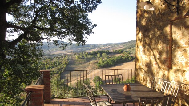 Un patio exterior con una mesa y sillas, vistas al campo y un muro de piedra.