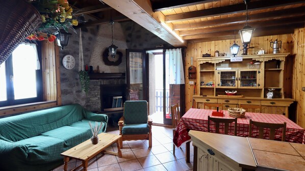 Un ambiente accogliente con un divano verde, un tavolo di legno, una sedia, un camino e pensili in legno con stoviglie.