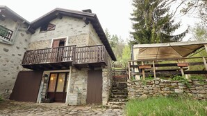 Un edificio de piedra con un balcón de madera, una escalera de madera y un área de estar al aire libre cubierta.