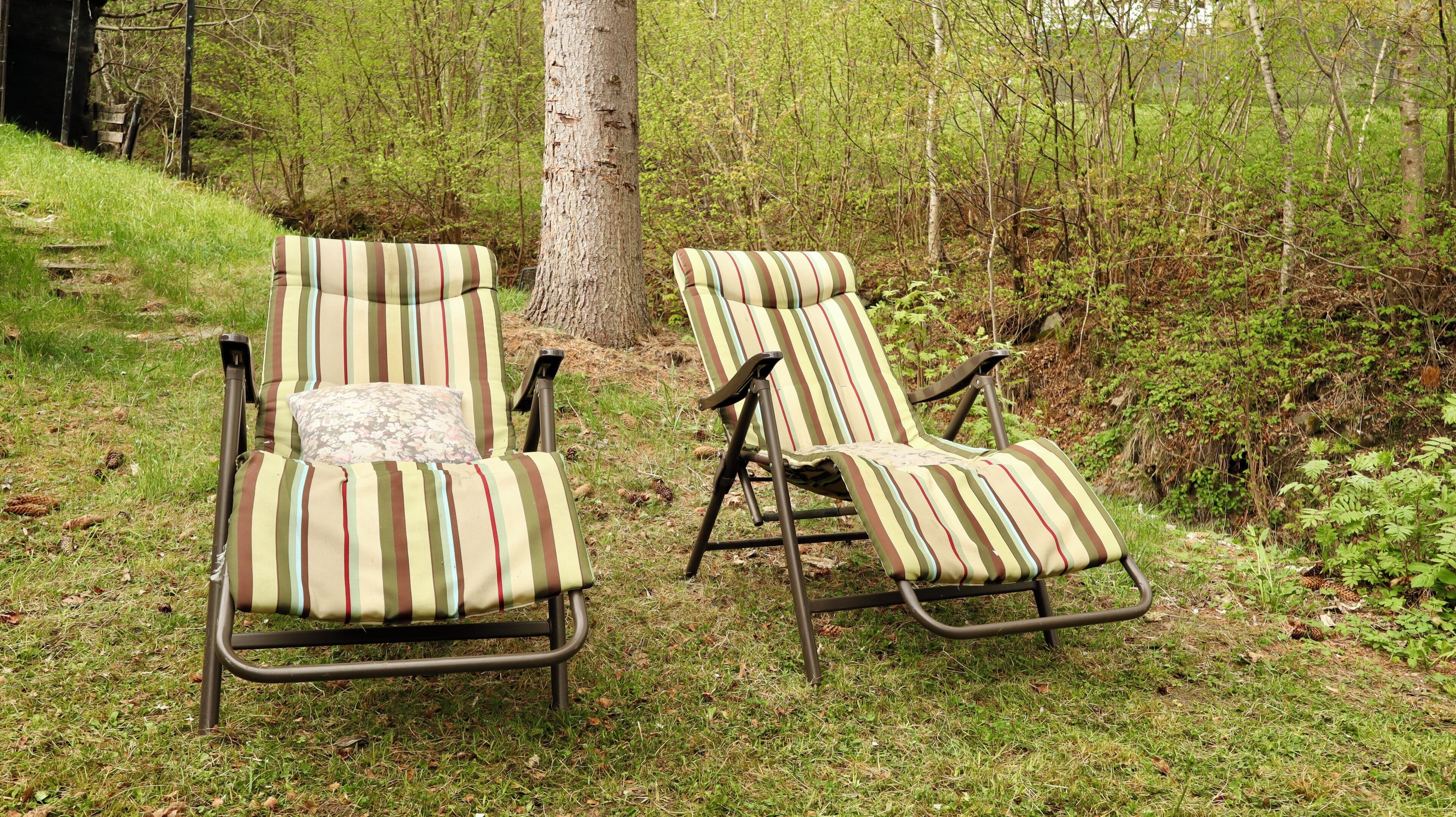 Two striped lounge chairs with metal frames, positioned on a grassy area with trees in the background.