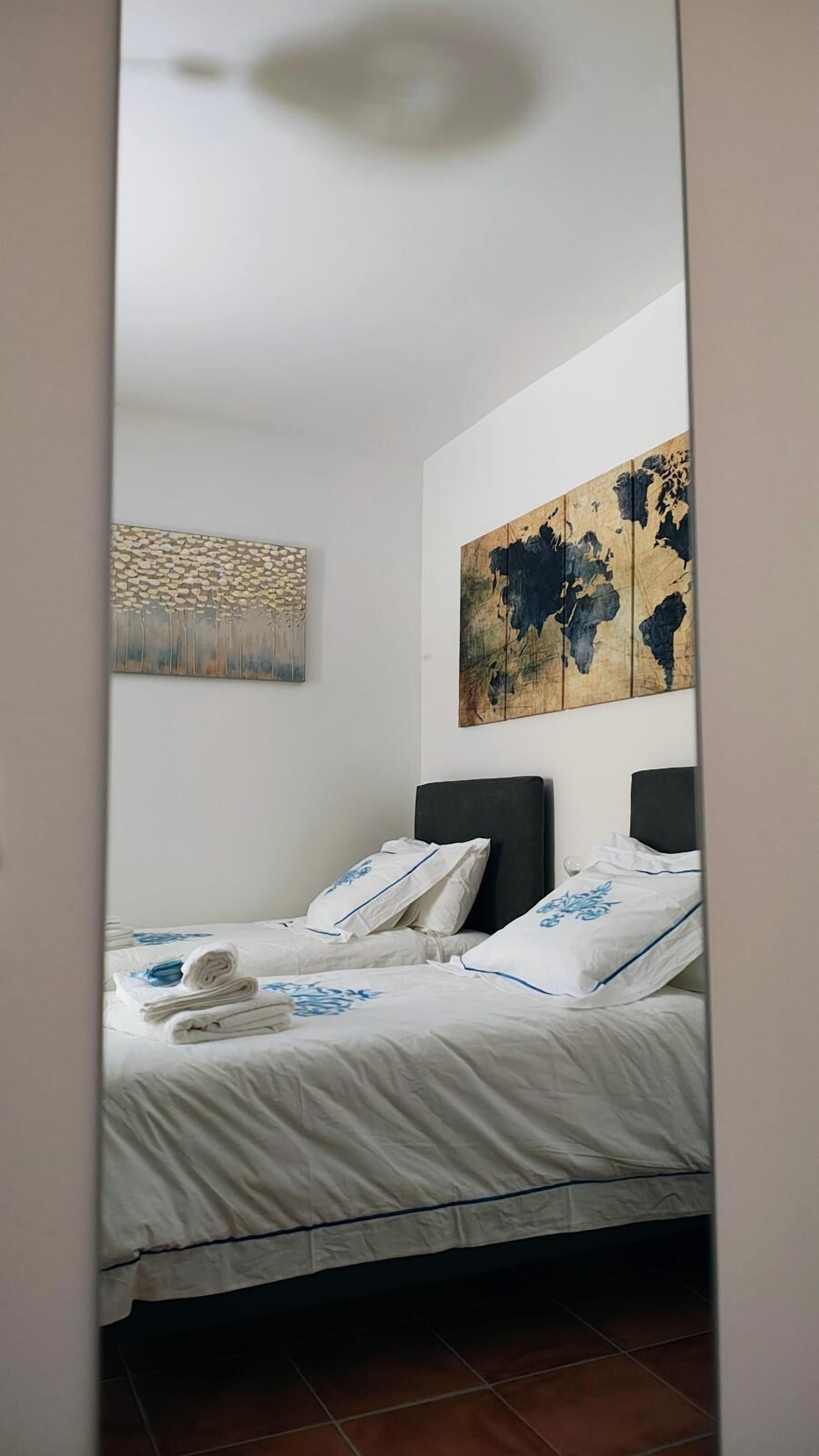 Una camera da letto con due letti, lenzuola bianche e un quadro raffigurante una mappa del mondo.
