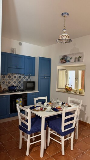 A dining area with a white table and chairs, a kitchen with blue cabinets, a microwave, and a decorative ceiling light. - LO ZECCHINO VACATION HOME (Archi)