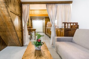 Una habitación acogedora con techo inclinado de madera, un sofá, una mesa de madera con una planta en maceta y una vista parcial de una cocina.