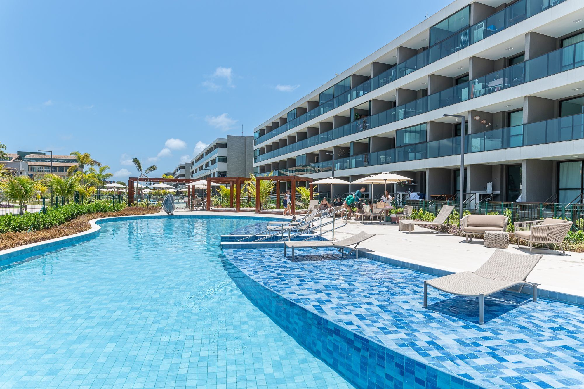 A modern hotel with a swimming pool, outdoor seating, and a multi-story building.