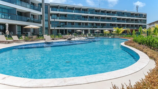 A modern hotel with a large pool, multiple balconies, and outdoor seating. - Beachclasssummer #c215 - Studio by Carpediem (Ipojuca)