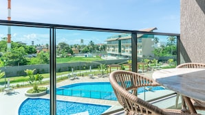 A balcony with a view of a swimming pool, lounge chairs, and a building in the background. - Beachclasssummer #c215 - Studio by Carpediem (Ipojuca)