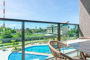 A balcony with a view of a swimming pool, lounge chairs, and a building in the background. - Beachclasssummer #c215 - Studio by Carpediem (Ipojuca)