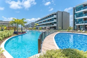 A modern hotel with a large swimming pool, multiple balconies, and a well-maintained garden area. - Beachclasssummer #c215 - Studio by Carpediem (Ipojuca)