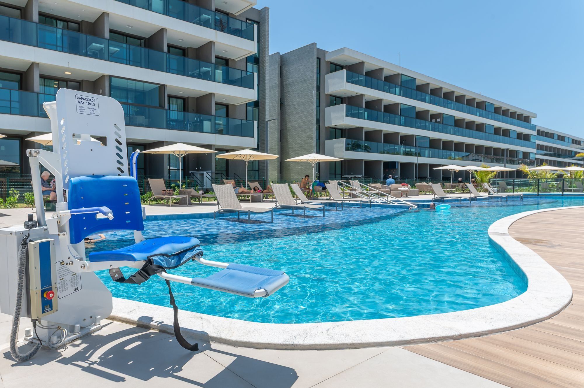 A swimming pool with lounge chairs and umbrellas, surrounded by a modern building with multiple balconies.