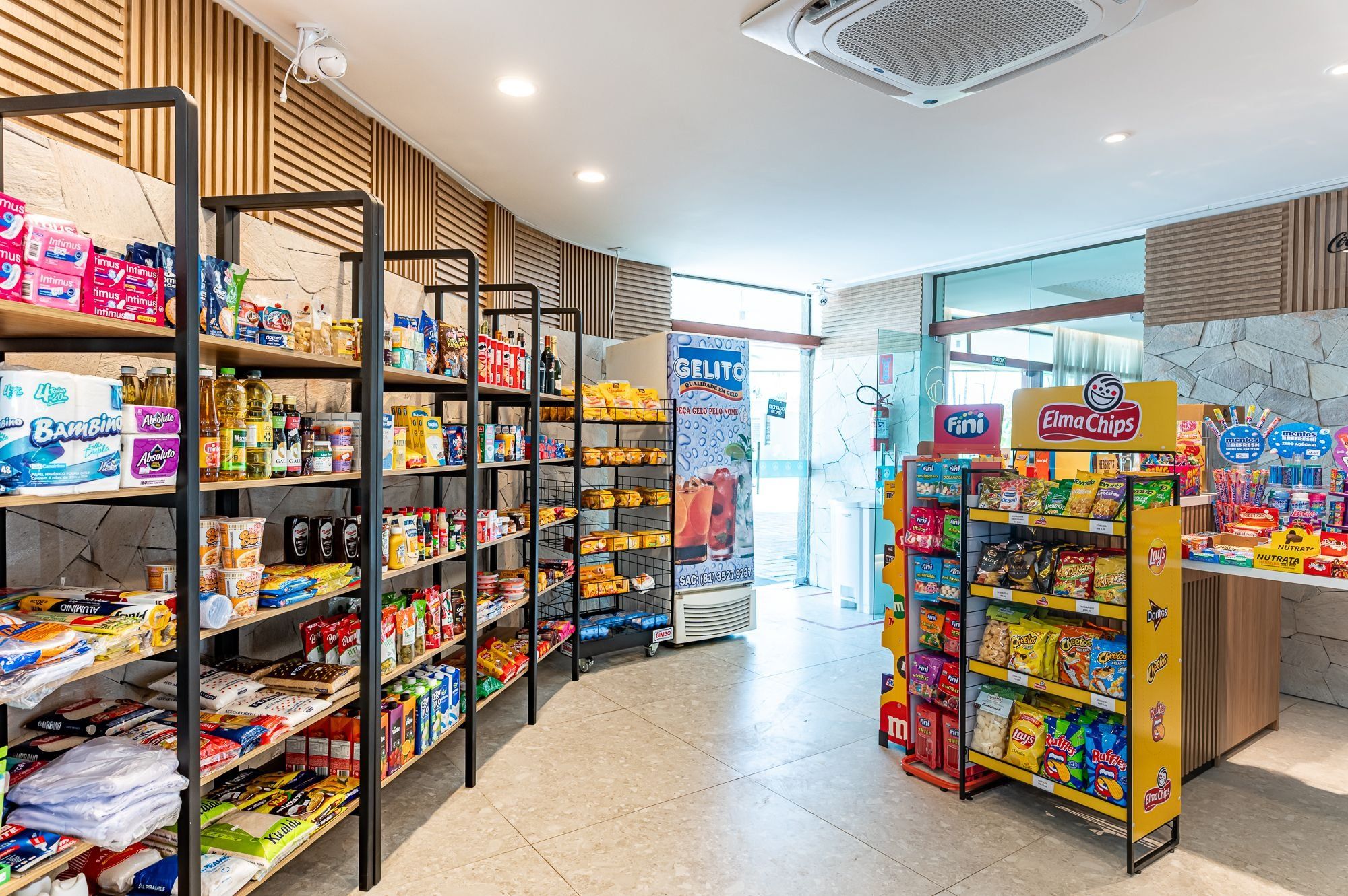 Un pasillo de un supermercado con estantes llenos de diversos productos, un congelador y una exhibición de aperitivos.