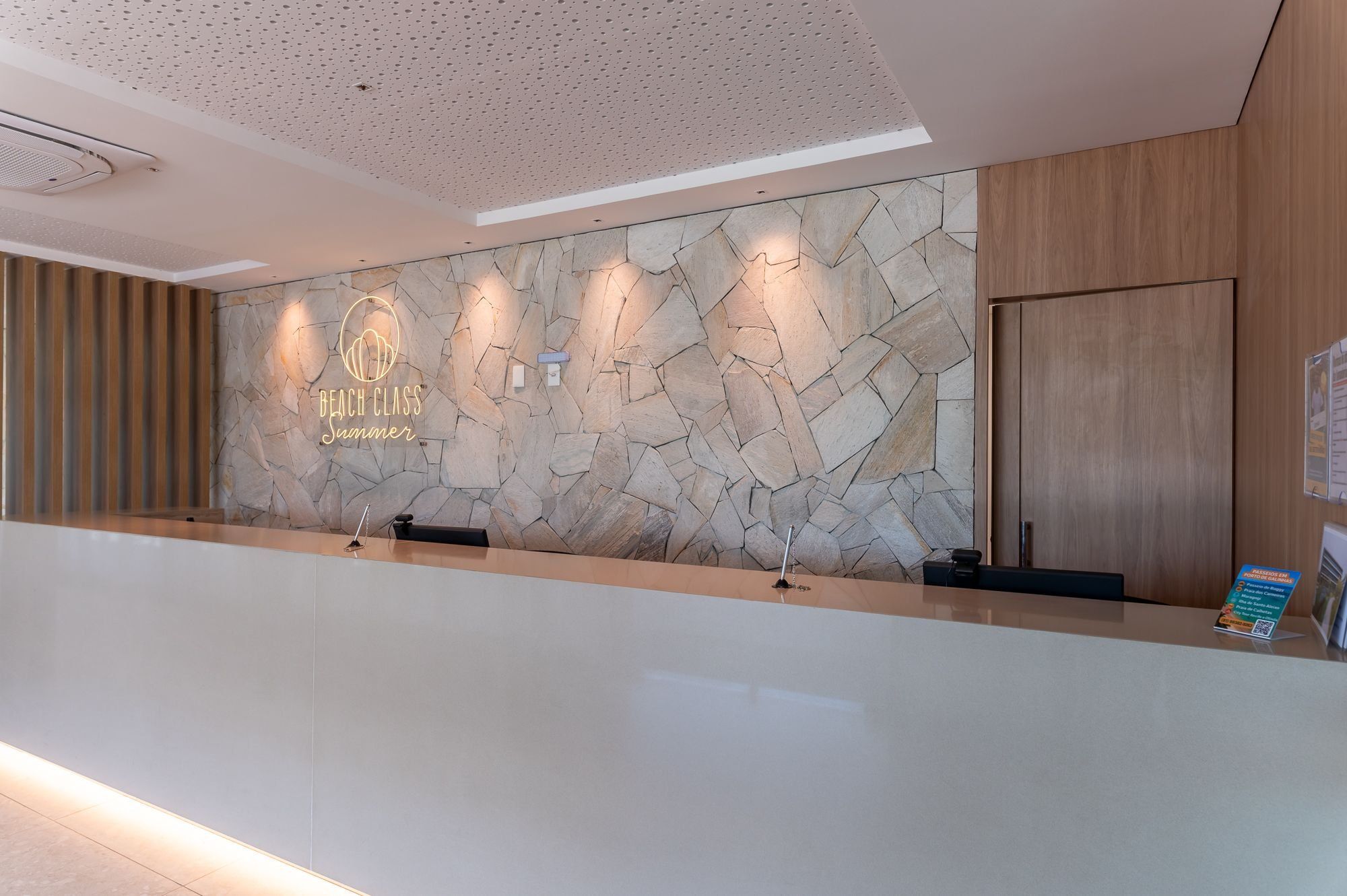 Un mostrador de recepción con un fondo de pared de piedra, un logotipo y un panel de madera a la derecha.