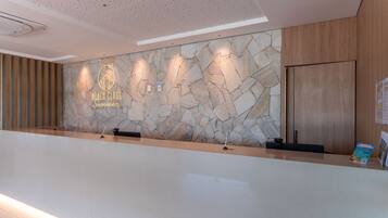 Un mostrador de recepción con un fondo de pared de piedra, un logotipo y un panel de madera a la derecha.