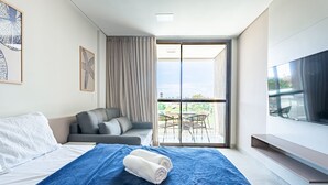 Une chambre d’hôtel moderne équipée d’un lit, d’un canapé, d’un balcon avec une table et des chaises, et d’une télévision.