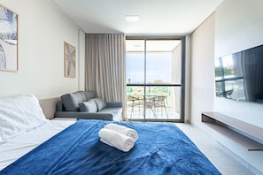 A modern hotel room with a bed, a sofa, a balcony with a table and chairs, and a TV. - Beachclasssummer #c215 - Studio by Carpediem (Ipojuca)