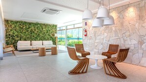 Un hall d’entrée moderne avec un mur végétal, un canapé blanc, des chaises en bois et un mur en pierre.