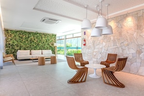 A modern lobby with a green wall, a white sofa, wooden chairs, and a stone wall. - Beachclasssummer #c215 - Studio by Carpediem (Ipojuca)