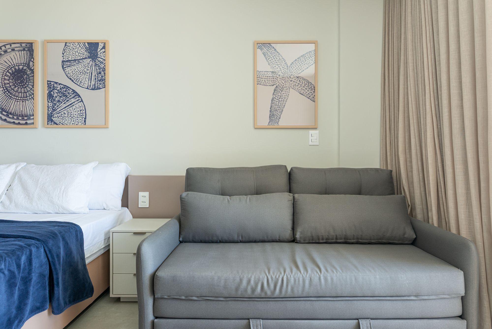 Un dormitorio con una cama, un sofá gris y dos obras de arte en la pared.
