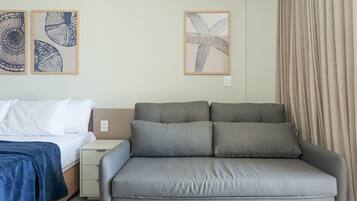 Un dormitorio con una cama, un sofá gris y dos obras de arte en la pared.