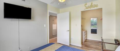 A bedroom with a bed, a ceiling fan, a TV mounted on the wall, and a door leading to another room.