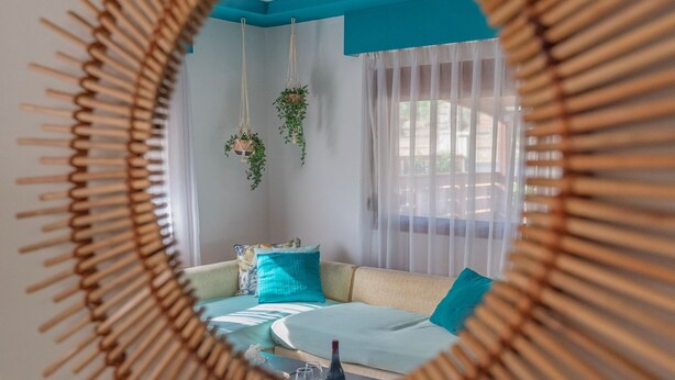 Ein Zimmer mit einem runden Spiegel, einer Couch mit Kissen, einer hängenden Pflanze und einem Fenster mit Vorhängen.