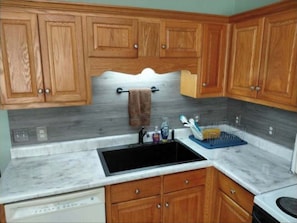 A kitchen with wooden cabinets, a black sink, and a marble countertop.