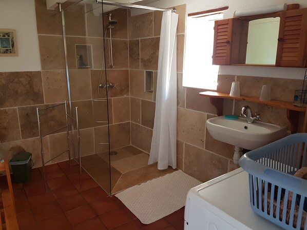 Een badkamer met een douchecabine van glas, een witte wasbak en een blauwe wasmand.