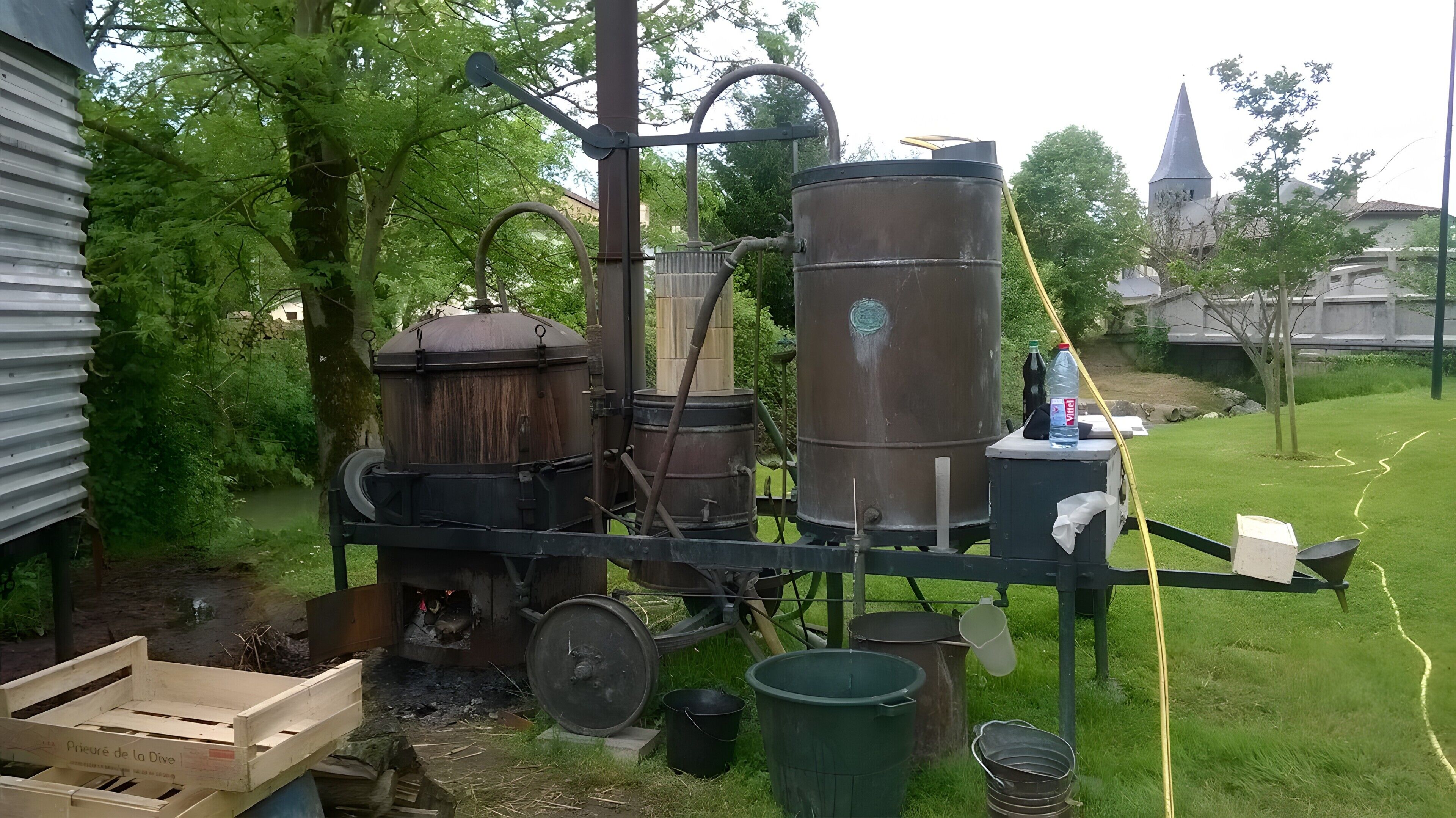 Ambiente industrial ao ar livre com grandes tanques de metal, caixas de madeira e uma área gramada.