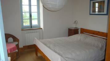 Ein Schlafzimmer mit einem hölzernen Bett, einem Fenster, einem Heizkörper, einem Sessel und einem Nachttisch.
