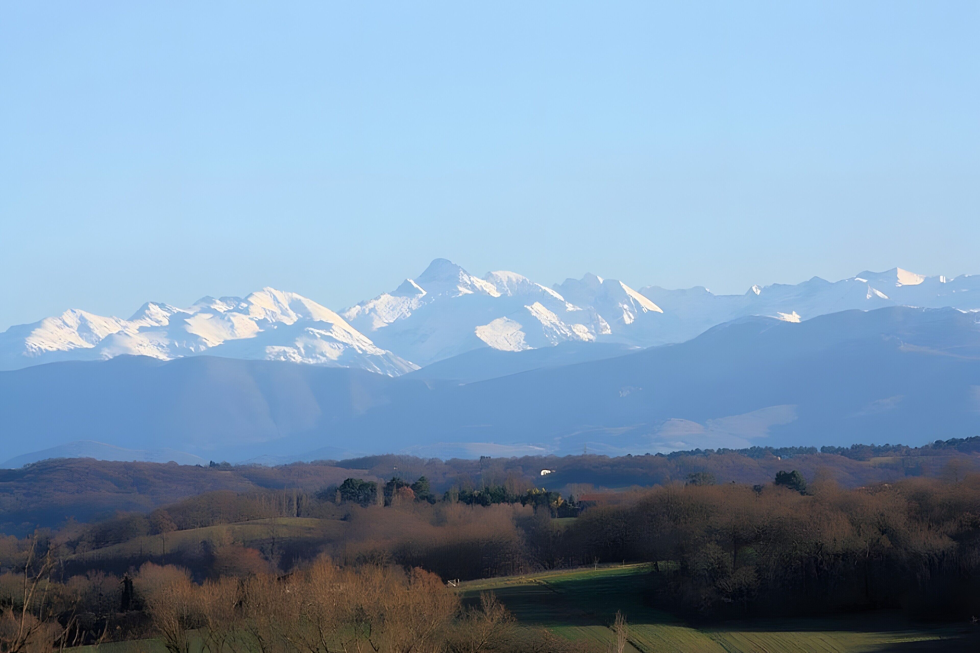 A mountain landscape with snow-capped peaks and a valley with trees and fields.