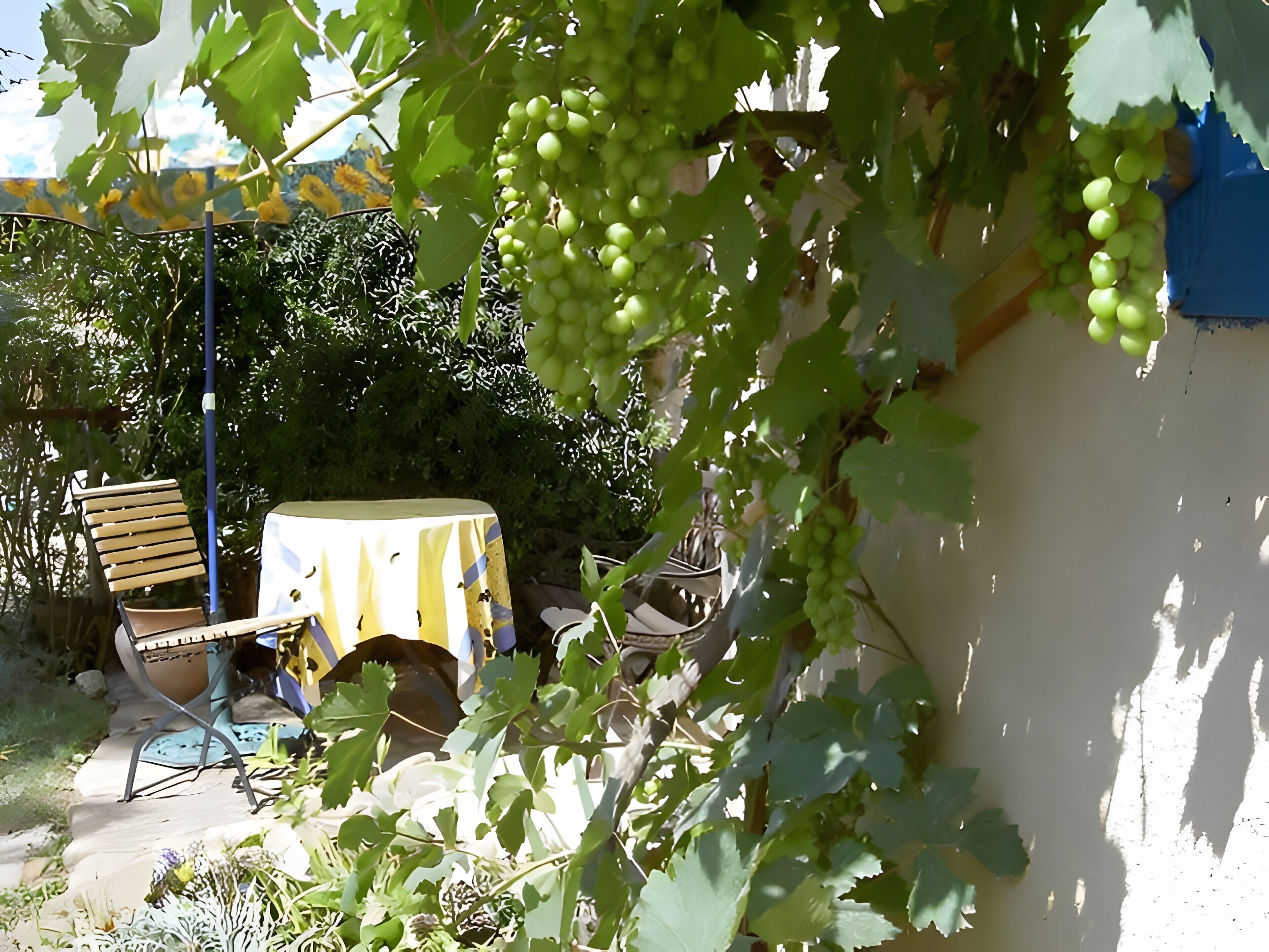 Un jardín con una mesa y sillas, un banco de madera y una pared con pintura descascarada.