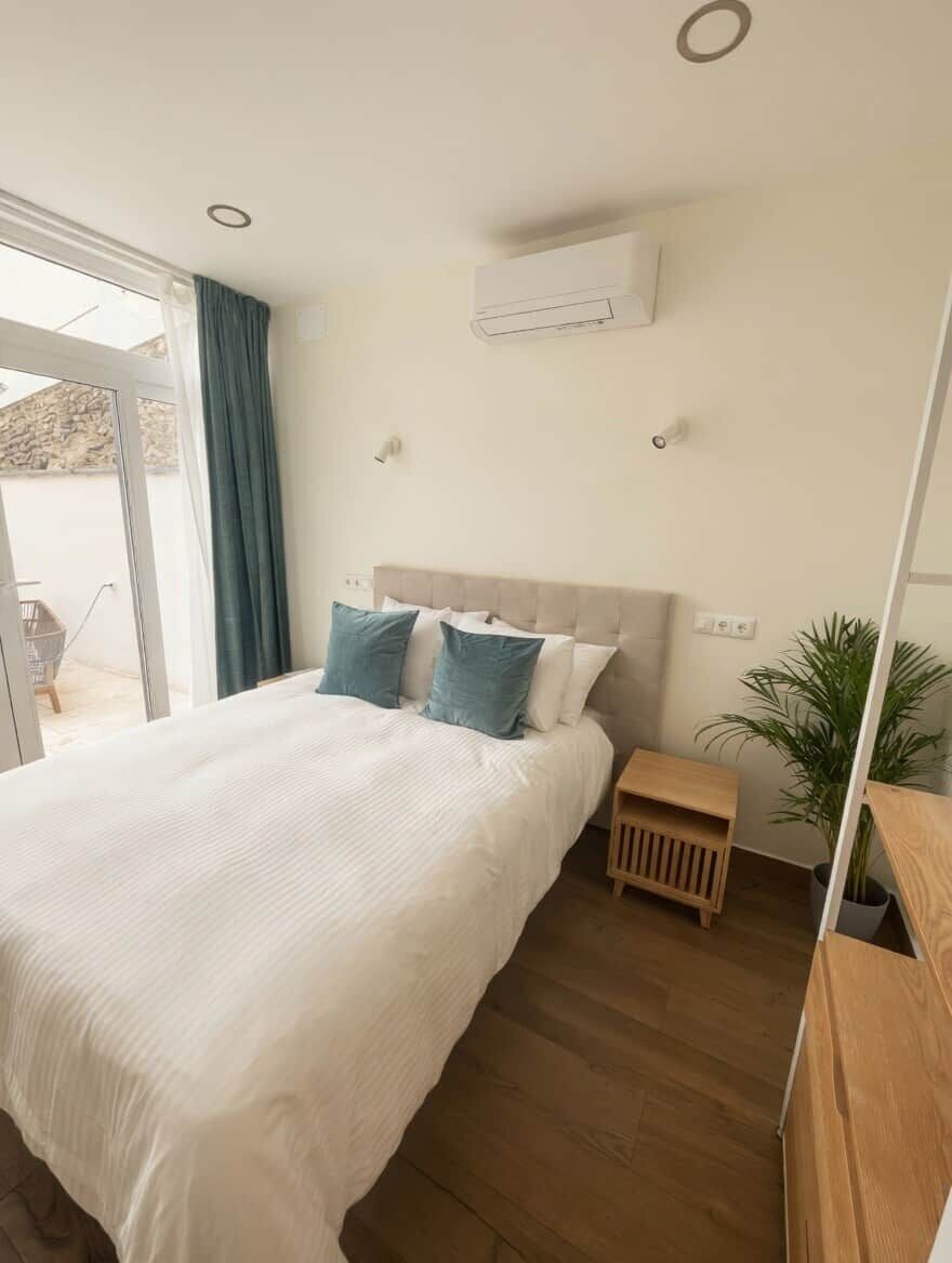 Una camera da letto con un letto grande, un comodino, una pianta in vaso e una porta scorrevole in vetro che dà su una zona esterna.