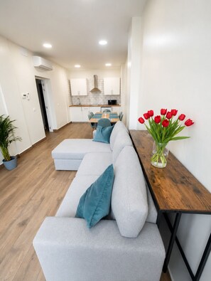 Un salon moderne avec un canapé d’angle gris, des coussins turquoise, une table basse en bois et un vase de tulipes rouges.