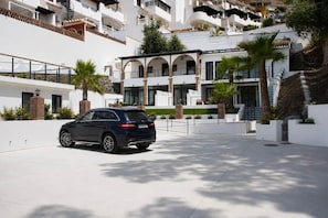 Un bâtiment moderne avec une voiture garée devant, entouré de murs blancs et de verdure.