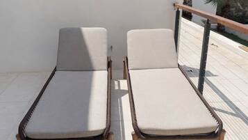 Dos sillones con cojines en un patio empedrado con baranda y vistas a un edificio con escaleras.