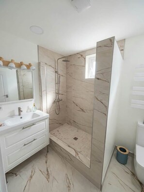 Une salle de bain avec un meuble-lavabo blanc, une cabine de douche en verre et un sol en marbre.