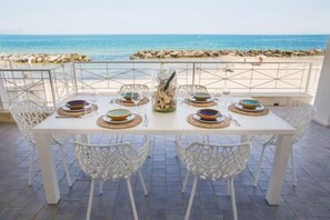 A dining table set with plates, glasses, and cutlery, overlooking a beach with rocks and the sea. - Riva Estate Villa by LeDhome   (Trappeto)