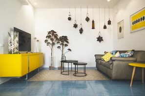 A living room with a yellow cabinet, a grey sofa, two small tables, hanging star-shaped lights, and a large TV. - Riva Estate Villa by LeDhome (Trappeto)