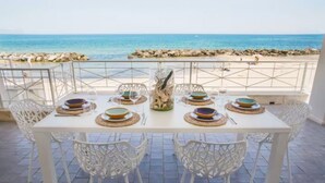 A dining table set with plates, glasses, and cutlery, overlooking a beach with rocks and the sea. - Riva Estate Villa by LeDhome (Trappeto)