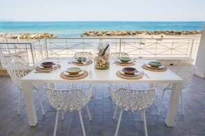 A dining table set with plates, glasses, and cutlery, overlooking a beach with rocks and the sea. - Riva Estate Villa by LeDhome (Trappeto)