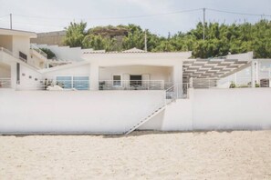 A coastal building with a staircase leading to a covered area, surrounded by sand and greenery. - Riva Estate Villa by LeDhome   (Trappeto)