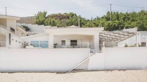 A coastal building with a staircase leading to a covered area, surrounded by sand and greenery. - Riva Estate Villa by LeDhome (Trappeto)