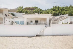 A coastal building with a staircase leading to a covered area, surrounded by sand and greenery. - Riva Estate Villa by LeDhome (Trappeto)